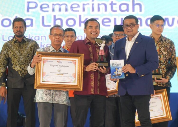 Menteri Ekonomi Kreatif Republik Indonesia, Teuku Riefky Harsya, didampingi oleh Pimpinan Perusahaan Serambi Indonesia, Mohd Din, menyerahkan penghargaan Serambi Ekraf Awards 2025 kepada Wali Kota Lhokseumawe, Sayuti Abubakar